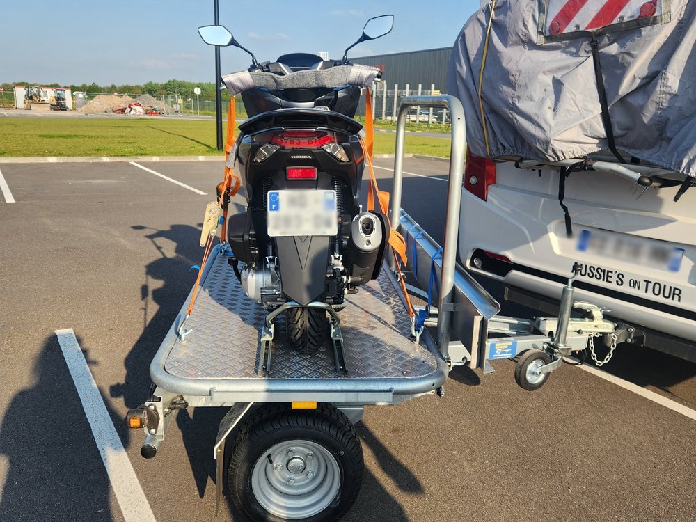 Honda PCX scooter secured on motorcycle trailer behind motorhome